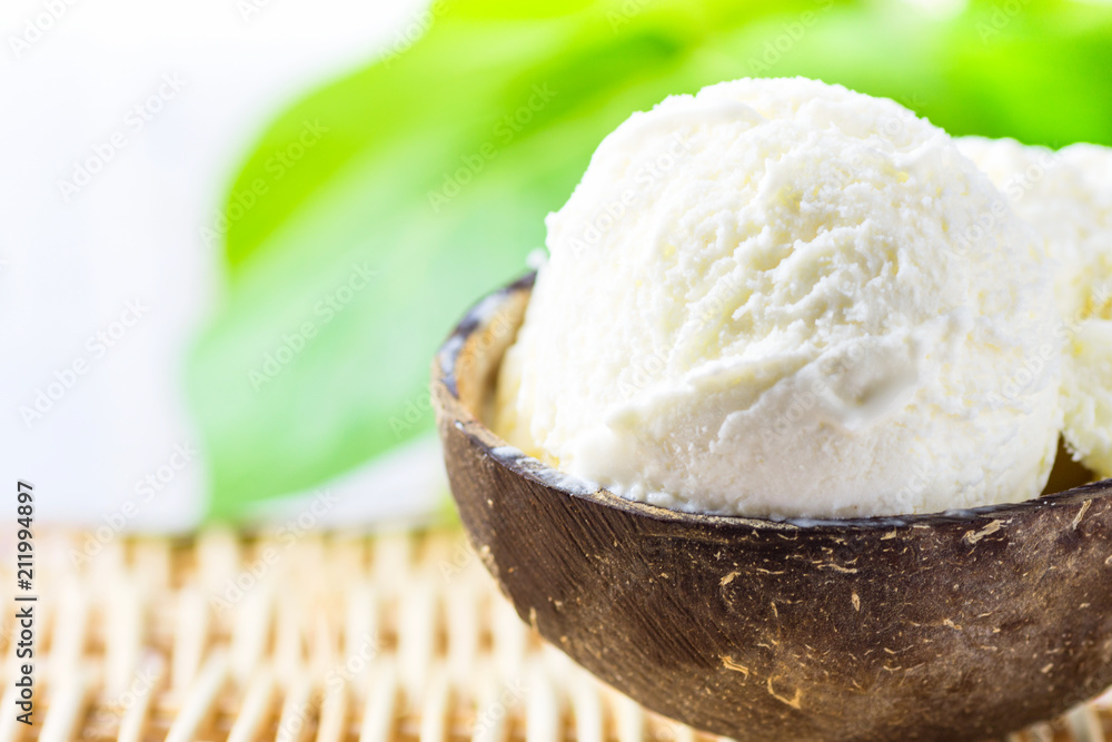 Scoop of Delicious Vegan Ice Cream in Coconut Bowl on Rattan Table. Green Palm Leaves Tropical Background. Plant Based Diet Healthy Dessert Superfoods. Vacation Concept. Copy Space
