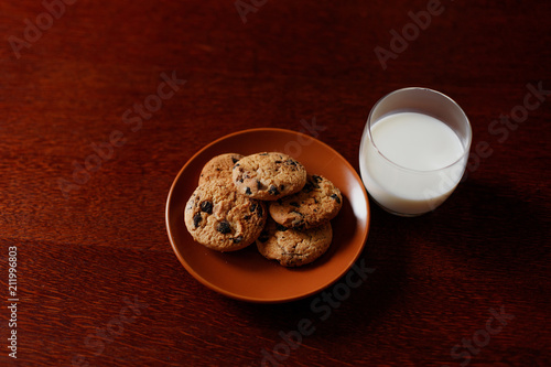 A glass of fresh milk and oatmeal cookies on a wooden table.