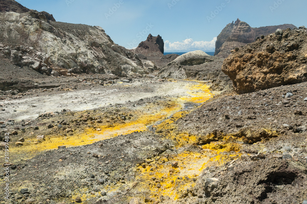 Obraz premium The outlet stream from the crater lake of the active volcano of White Island, Whakaari, off the Bay of Plenty coast, New Zealand. Yellow crystals of sulphur in the foreground.