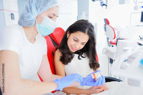 Young girl dentist in mask shows young beautiful girl dentures.