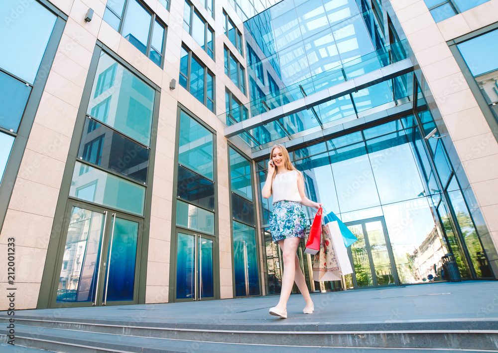 Lifestyle portrait young blonde girl, with shopping bags walking out from shop and talking by mobile phone. Lifestyle portrait young blonde girl, with shopping bags walking out from shop and talking by mobile phone.