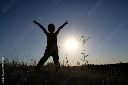 Silhouette of a boy with his hands up in the pose of a rune man. The child joyfully meets the dawn of the sunrise.