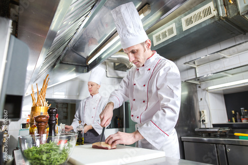 Chef cutting meat on chopping board, professional cook holding knife and cutting meat in restaurant