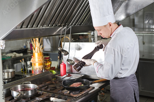 Chef in restaurant kitchen at stove with pan, cooking