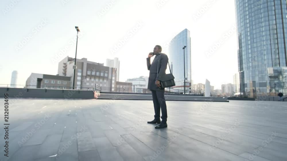 Zoom in of african american businessman standing in front of modern office building in downtown at having phone conversation Zoom in of african american businessman standing in front of modern office building in downtown at having phone conversation