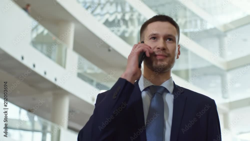 Low angled shot of young handsome man talking on mobile phone while walking through hall of large modern business center Low angled shot of young handsome man talking on mobile phone while walking through hall of large modern business center