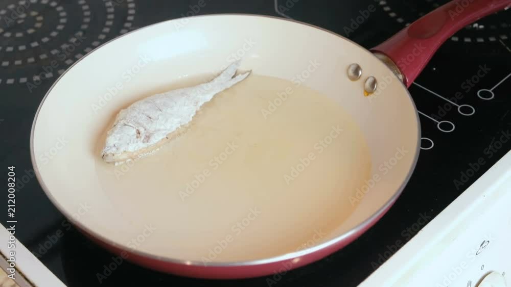 Man frying carps fish on a frying pan with oil. Close-up man's hand putting a fish on frying pan. Man frying carps fish on a frying pan with oil. Close-up man's hand putting a fish on frying pan.