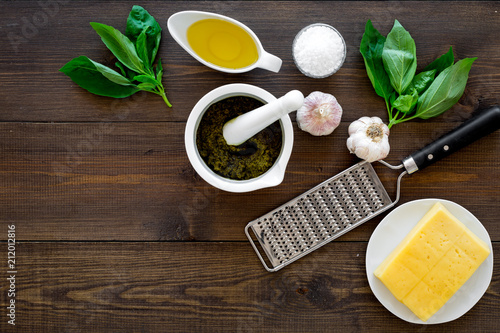 Fototapeta Naklejka Na Ścianę i Meble -  Ingredients for pesto sauce. Cheese, garlic, green basil, olive oil, salt near grater and mortar on dark wooden background top view copy space