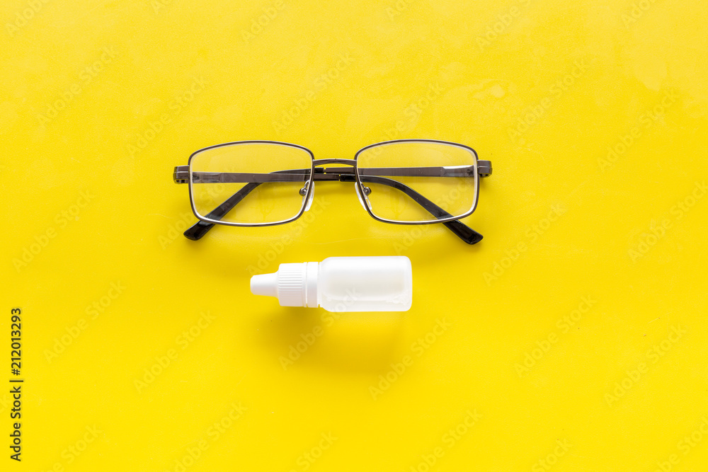 Eye drops in small bottle near glasses on yellow background top view copy space Eye drops in small bottle near glasses on yellow background top view copy space