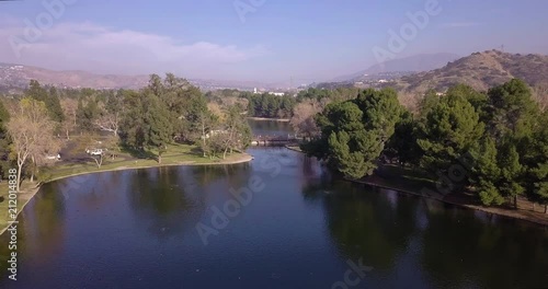 Aerial footage flying through a beautiful park with lake, family and some far off city views in Yorba Linda, CA