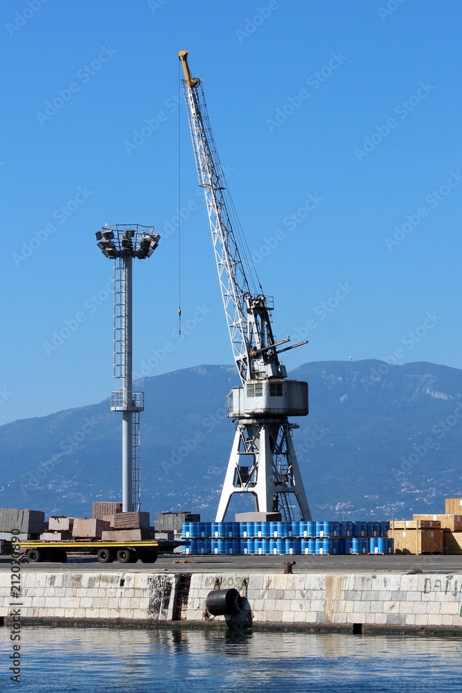 Old rusted shipyard loading crane located at the end of pier and still ready for loading and unloading while standing proudly on a warm sunny day