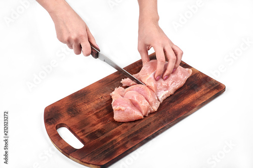 Cutting raw meat with a kitchen knife on a cutting board isolated on white background