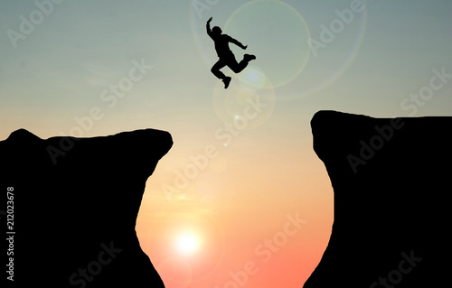 Silhouette concept idea. A man jumping over cliff on sunset background. A man jumping between the rock mountains. Freedom , active 