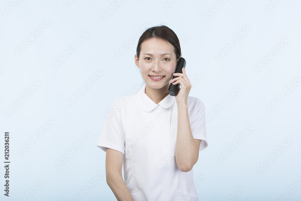 電話の受話器を持って微笑む白衣を着た女性 電話の受話器を持って微笑む白衣を着た女性