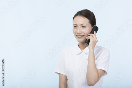 電話の受話器を持って微笑む白衣を着た女性