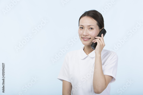 電話の受話器を持って微笑む白衣を着た女性