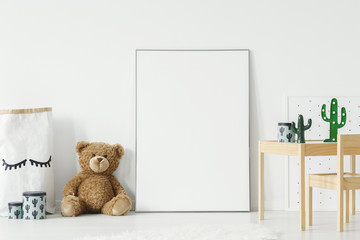Mockup poster, teddy bear and material basket placed on the floor in white room interior with wooden table and small chair. Paste your photo here