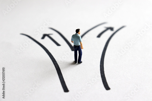 A miniature man standing in front of two roads.