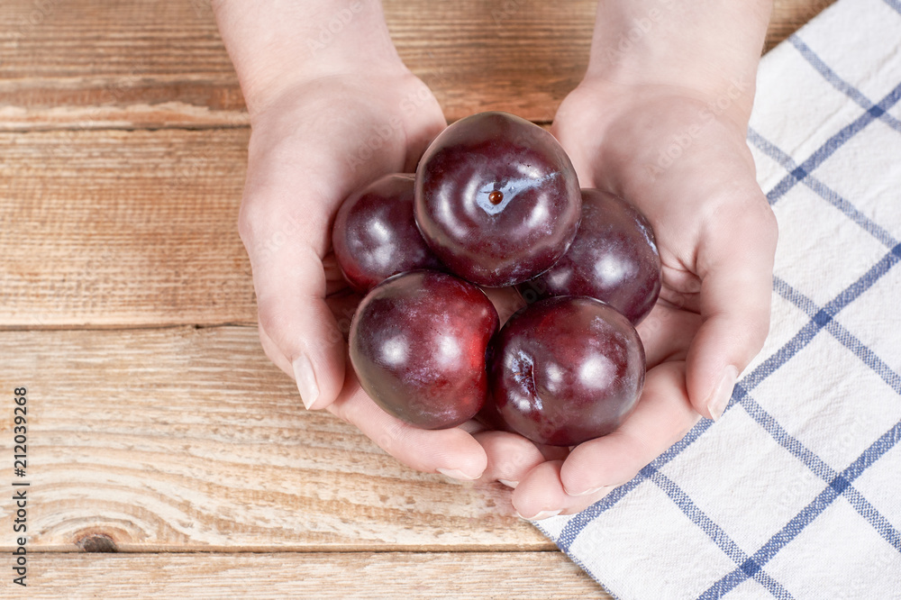 female hands holds few red plums next to a doily with figure on a wooden background female hands holds few red plums next to a doily with figure on a wooden background
