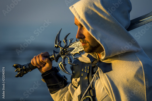 Portrait of assassin in white costume with the sword at the sea. He is posing...
