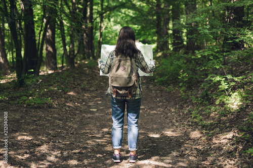 Young woman with backpack and map on forest path on summer day. Girl with tourist backpack travels.