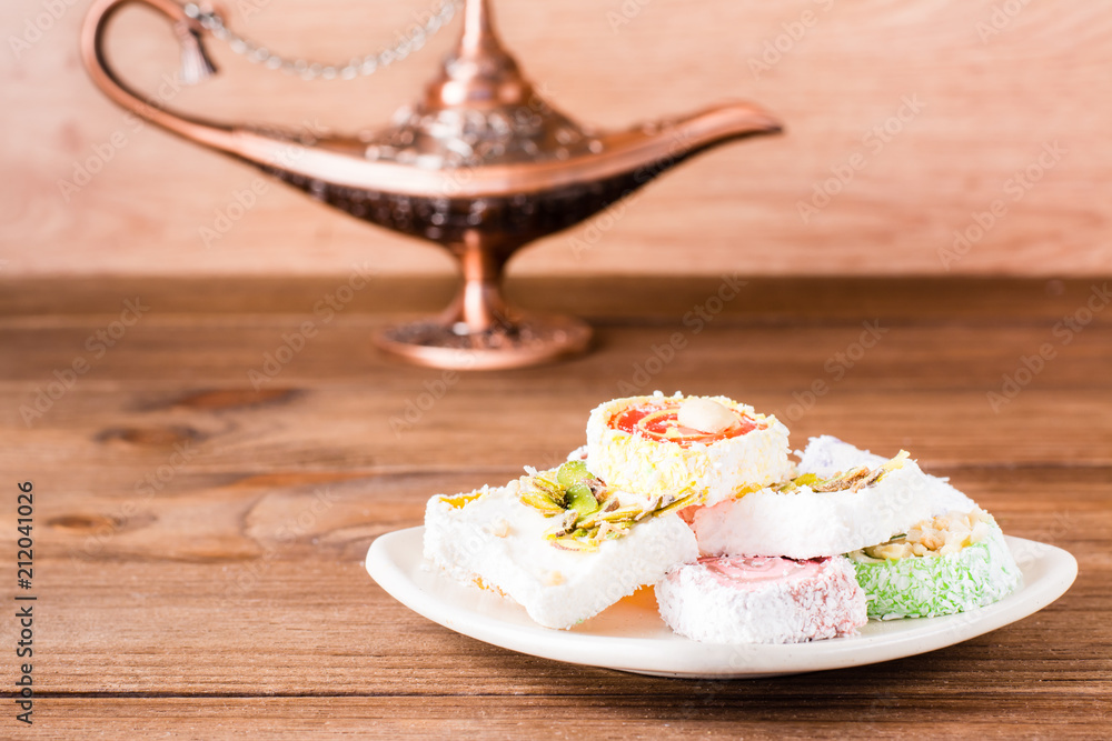 Traditional Turkish Delight on a plate and aladdin lamp on a wooden table.