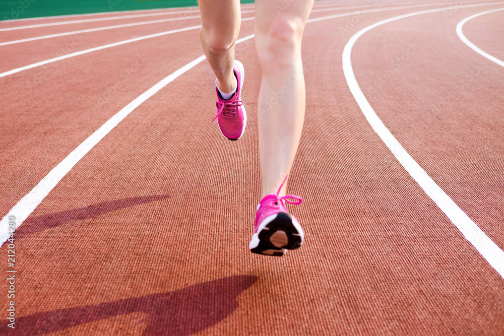 Athletic young woman in pink sneakers run on running track stadium