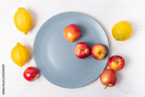 Fresh apples and lemons in a plate on white background.