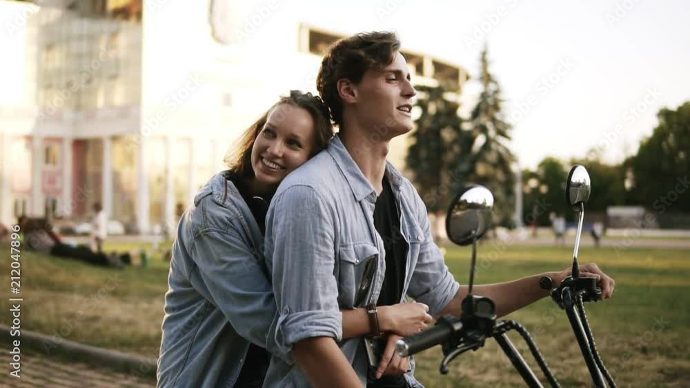 Young attractive couple hugging and enjoying themselves while sitting on a bike on the street. Both wearing blue shirts. Sunlight Young attractive couple hugging and enjoying themselves while sitting on a bike on the street. Both wearing blue shirts. Sunlight
