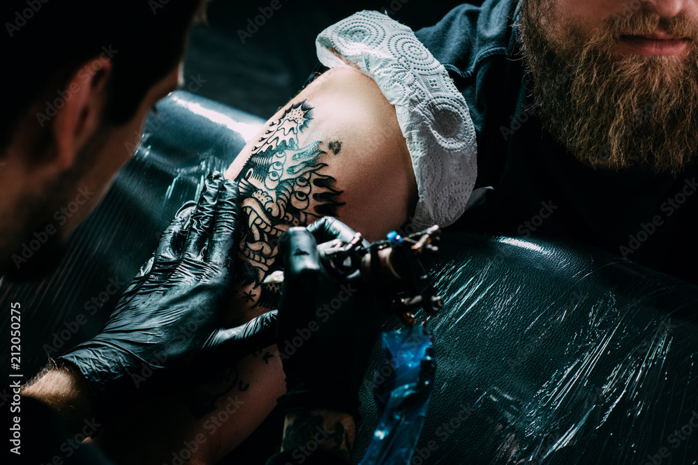 Φωτογραφία cropped shot of tattoo artist in gloves working on tattoo on shoulder in salon