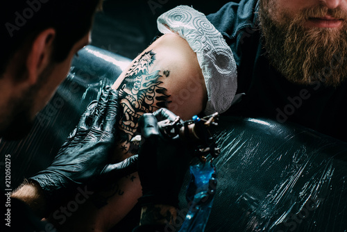 cropped shot of tattoo artist in gloves working on tattoo on shoulder in salon photo