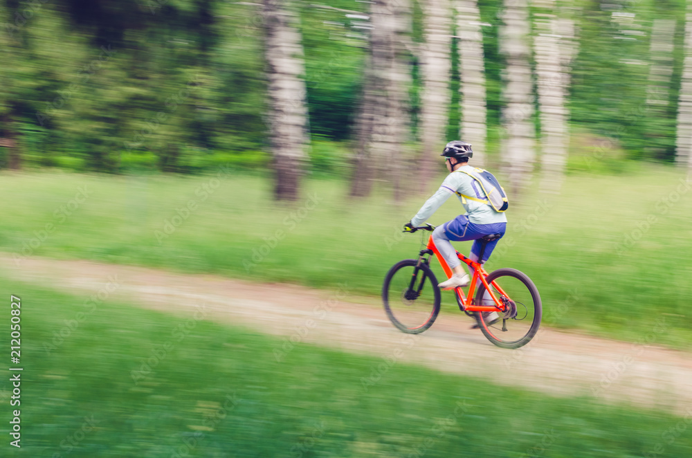 A cyclist in a helmet rides through the forest on a bicycle path, motion blur A cyclist in a helmet rides through the forest on a bicycle path, motion blur