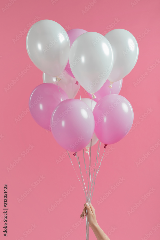Cropped view of holding pink and white balloons in girl hand isolated on pink