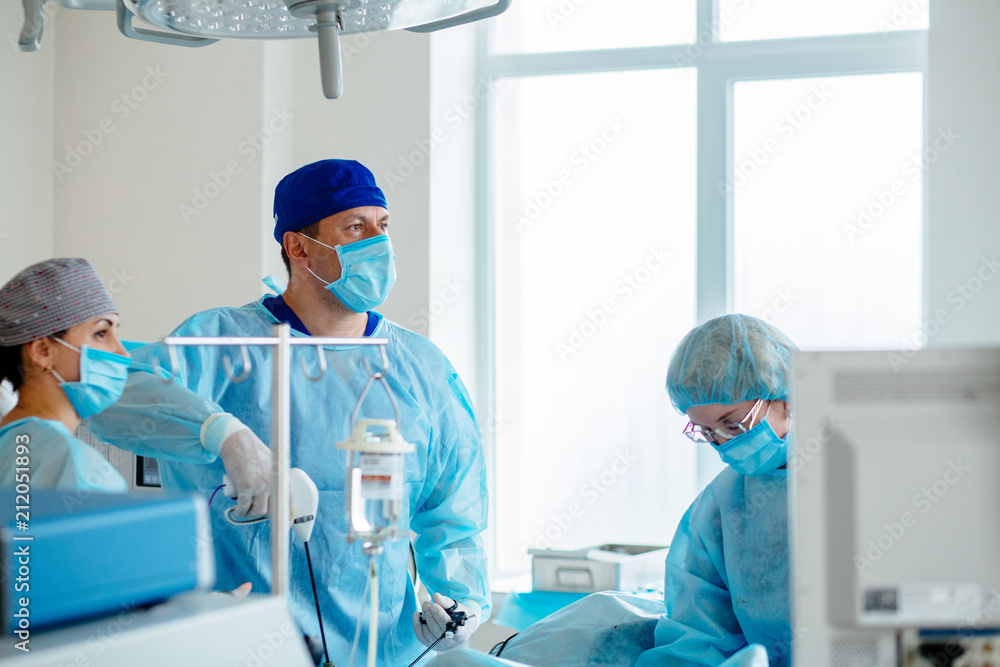 Surgeons team preforming operation in hospital operating theater, male surgeon operating patient,wearing surgical gown,operating room,,working with surgical laparoscopy instruments. Gynecology. Surgeons team preforming operation in hospital operating theater, male surgeon operating patient,wearing surgical gown,operating room,,working with surgical laparoscopy instruments. Gynecology.