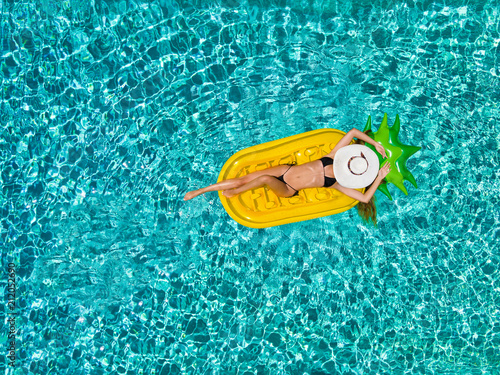 Urlaubskonzept einer jungen, attraktiven Frau die auf einer aufblasbaren Ananas über türkisem Wasser treibt