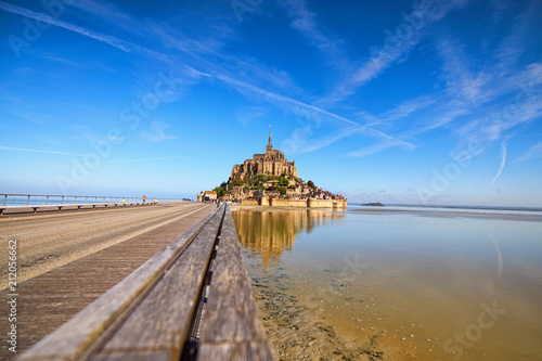 Road to Mont Saint Michel abbey. It is reflected in water. This is one of the most famous tourist attractions in France. Landscape photo during sunrise. Normandy, France