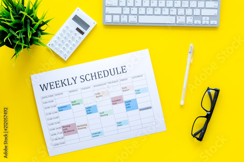 Weekly schedule of manager, office worker, pr specialist or marketing expert. Table with multicolored blocks on yellow office desk with computer, glasses, calculator top view photo