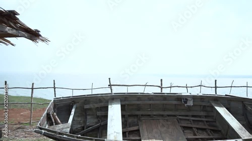 Panoramic view of village. Old dilapidated black wooden boat with a one-storey house, a well and a hill. Old wooden water well. Video photo