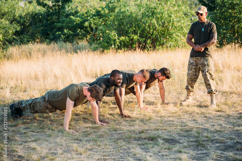 Foto tactical instructor in sunglasses examining multicultural soldiers doing push up