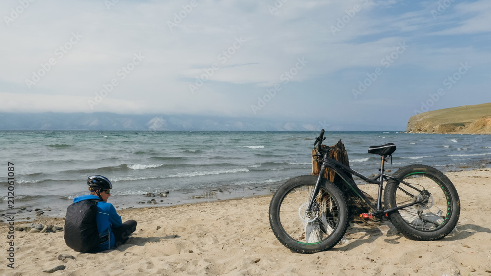 Obraz premium Fat bike also called fatbike or fat-tire bike in summer driving on the beach. The guy sits on the wheel of his bicycle, looks at the sea.