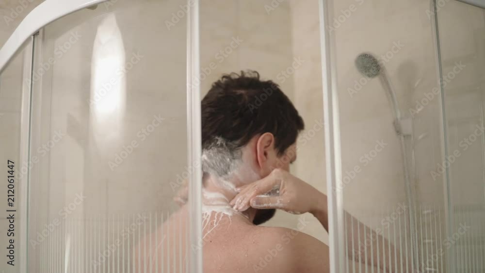a young and dark-haired man thoroughly cleanses his neck in order to freshen up and be clean, he stands in the shower in the bathroom and uses shampoo and water a young and dark-haired man thoroughly cleanses his neck in order to freshen up and be clean, he stands in the shower in the bathroom and uses shampoo and water