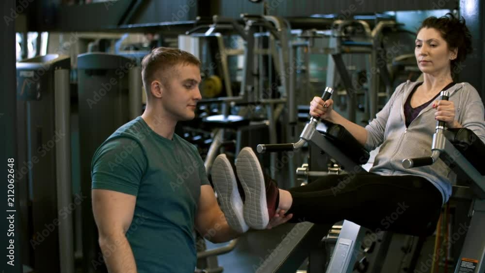 Tracking shot of attentive male fitness professional teaching woman to do leg raise exercise using dip station during workout at the gym Tracking shot of attentive male fitness professional teaching woman to do leg raise exercise using dip station during workout at the gym