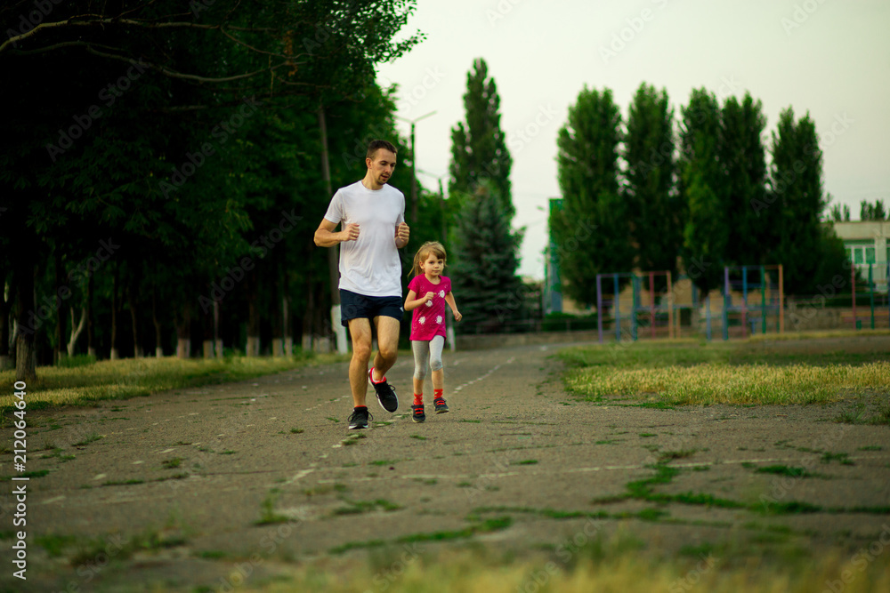 Athletic young father and little daughter running in stadium at sunset. Healthy lifestyle Athletic young father and little daughter running in stadium at sunset. Healthy lifestyle