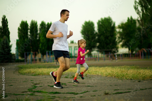 Athletic young father and little daughter running in stadium at sunset. Healthy lifestyle