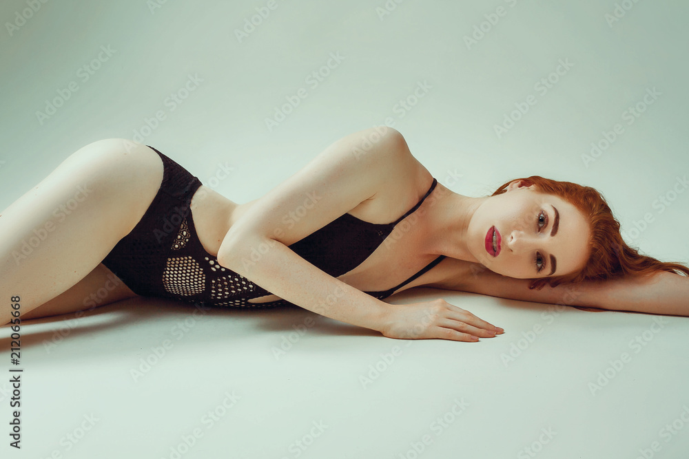 Model shoot in studio. Skinny girl with red long hair posing in the black  knitted swimsuit bikini lying on the floor Stock Photo | Adobe Stock