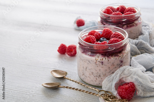 Chia milk pudding with raspberry in the glass jar with copy space for text. Decorated with fresh berries, vintage spoons and cloth. Summer detox superfoods breakfast or healthy dessert. Side view