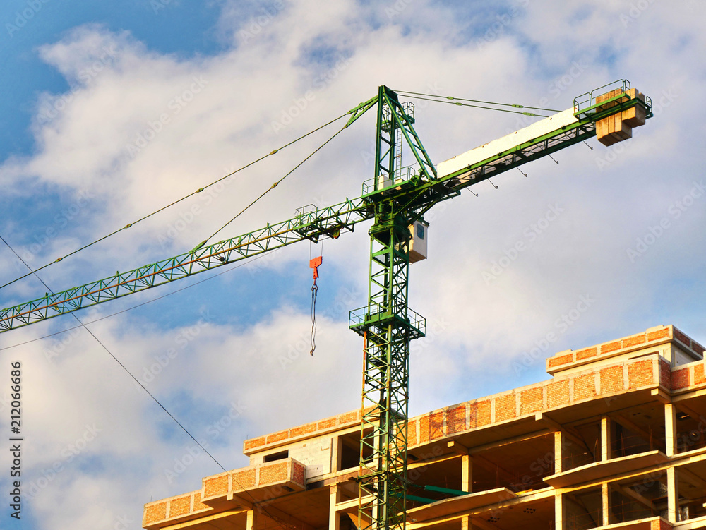 Crane near building against blue sky. Building under construction.