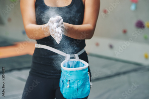Faceless shot of woman applying white dust of magnesia on hands before climbing wall in bouldering center photo