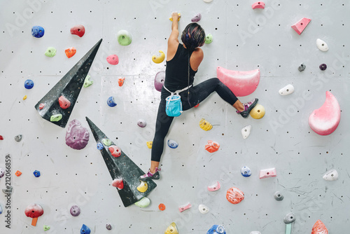 Back view of woman on climbing wall with colorful artificial elements in bouldering center