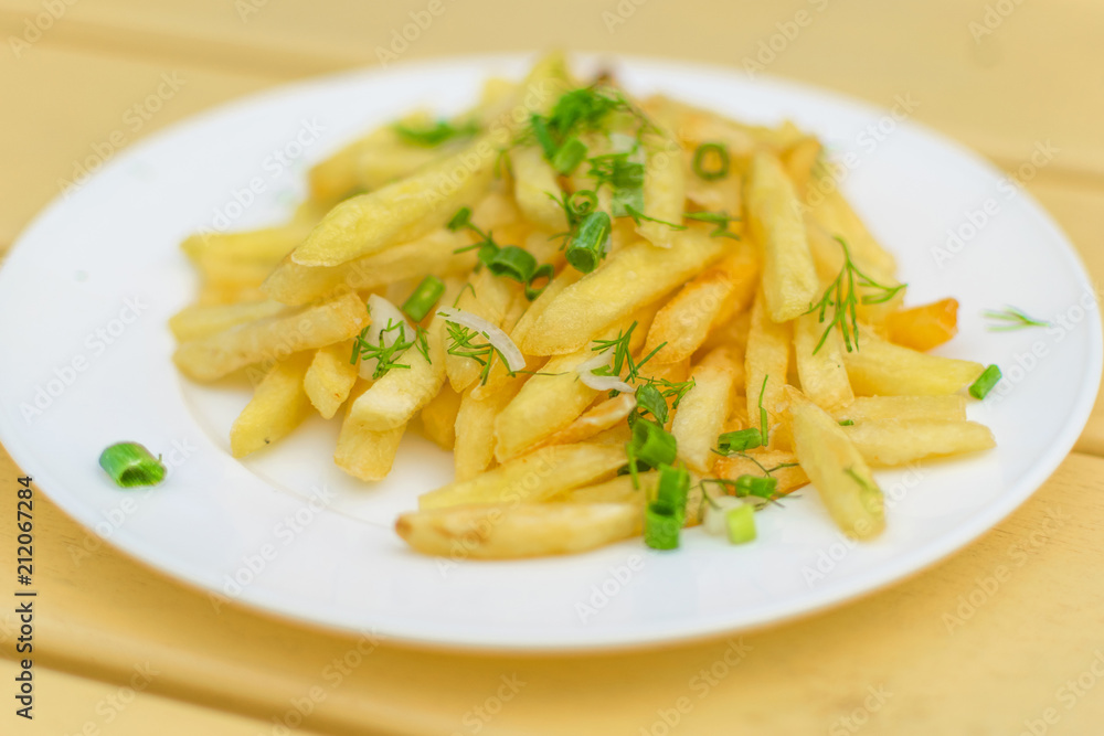 French fries on a plate on a yellow wooden background.